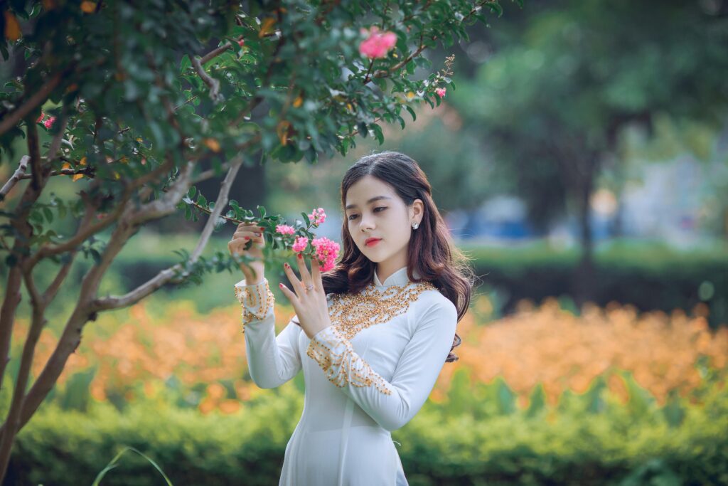 A cute girl standing in a garden next to a tree, looking thoughtfully.