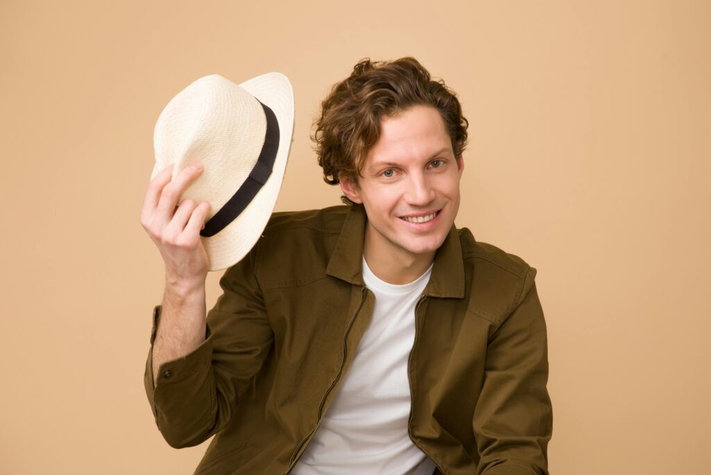 A man holding his cap and smiling as he stares at someone.