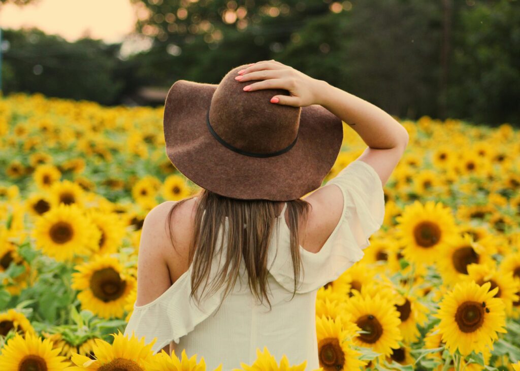 A girl standing in a sunflower field, wearing a cowboy hat and gazing into the distance.