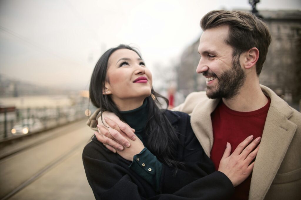 A couple standing in a park, smiling warmly at each other.