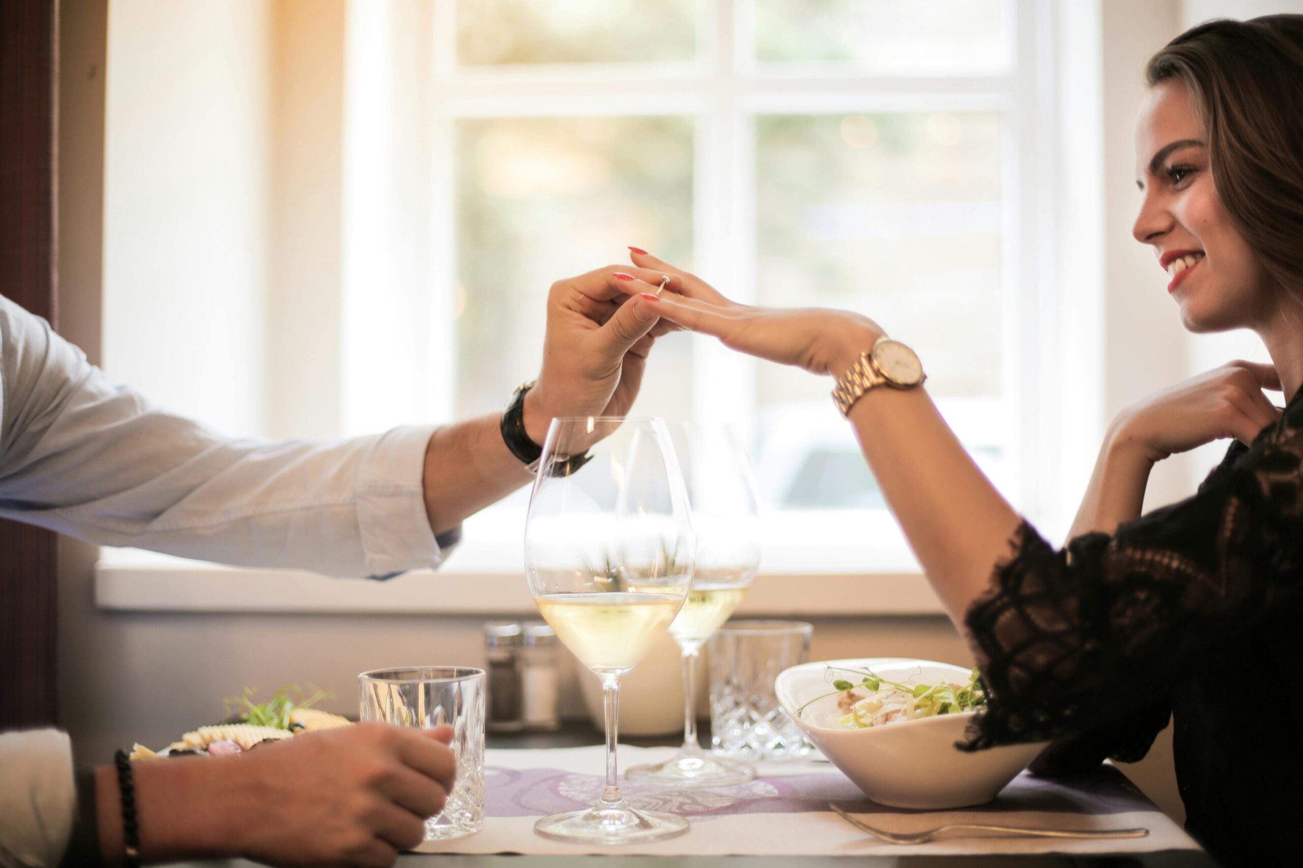 A couple sitting in a cozy cafe, with the man gently holding the woman's hand, while asking about her relationship status.