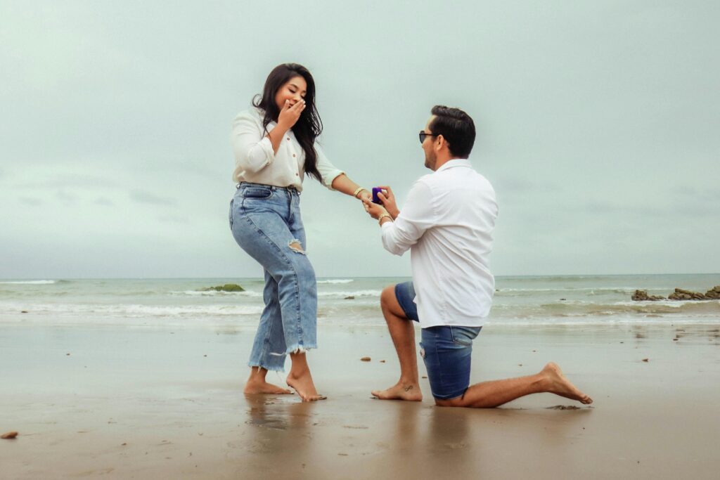 A boy proposing to his girlfriend at the beach, creating a memorable moment against the backdrop of the ocean.