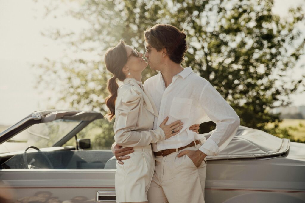 A couple on a road trip, standing together as the man kisses her neck affectionately.