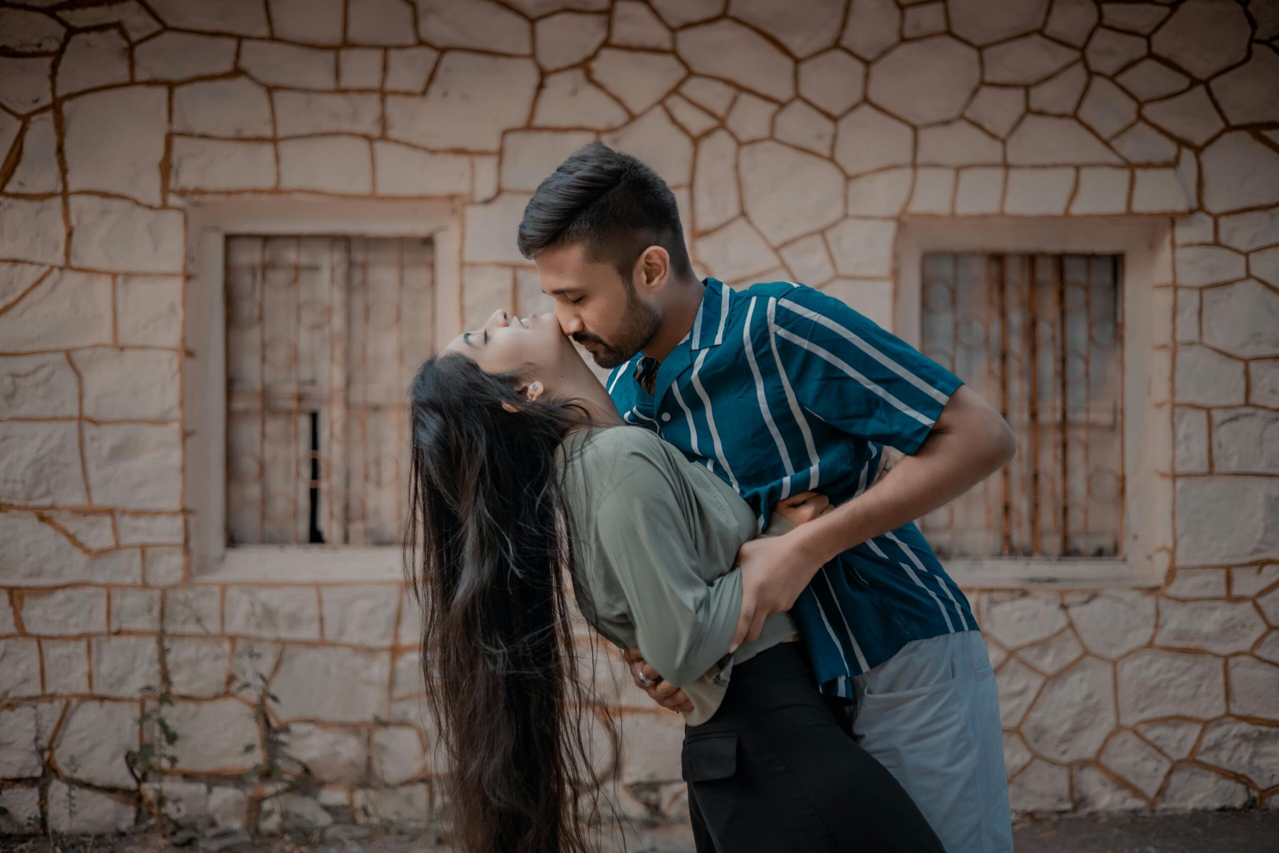 A couple standing at a historical site, with the boy kissing and gently biting her neck, pondering the meaning behind his affectionate gesture.