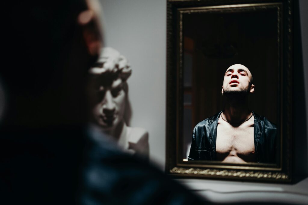 A man confidently looking at his chest in the mirror.