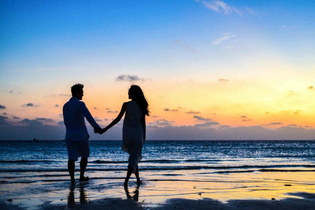 A couple enjoying the sunset on the beach, overlooking the ocean.