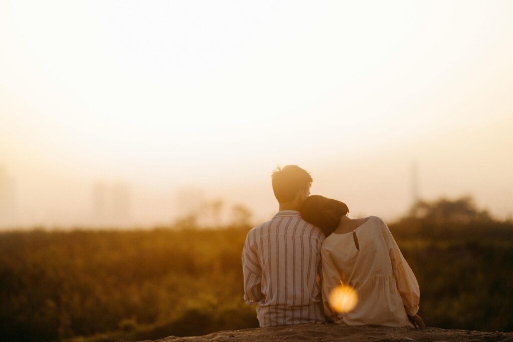 A couple sitting on a hill, watching the sunset together.