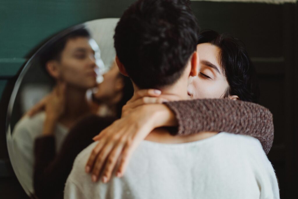 A couple standing in a room, with the girl kissing the boy.